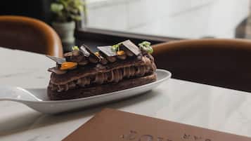 Una porción de pastel de chocolate sobre un plato blanco, decorado con trozos de chocolate y hojas encima, sobre una mesa de mármol.
