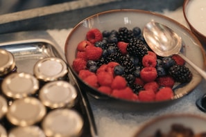 A bowl of fresh berries and a spoon sit on a surface, accompanied by a selection of round containers.