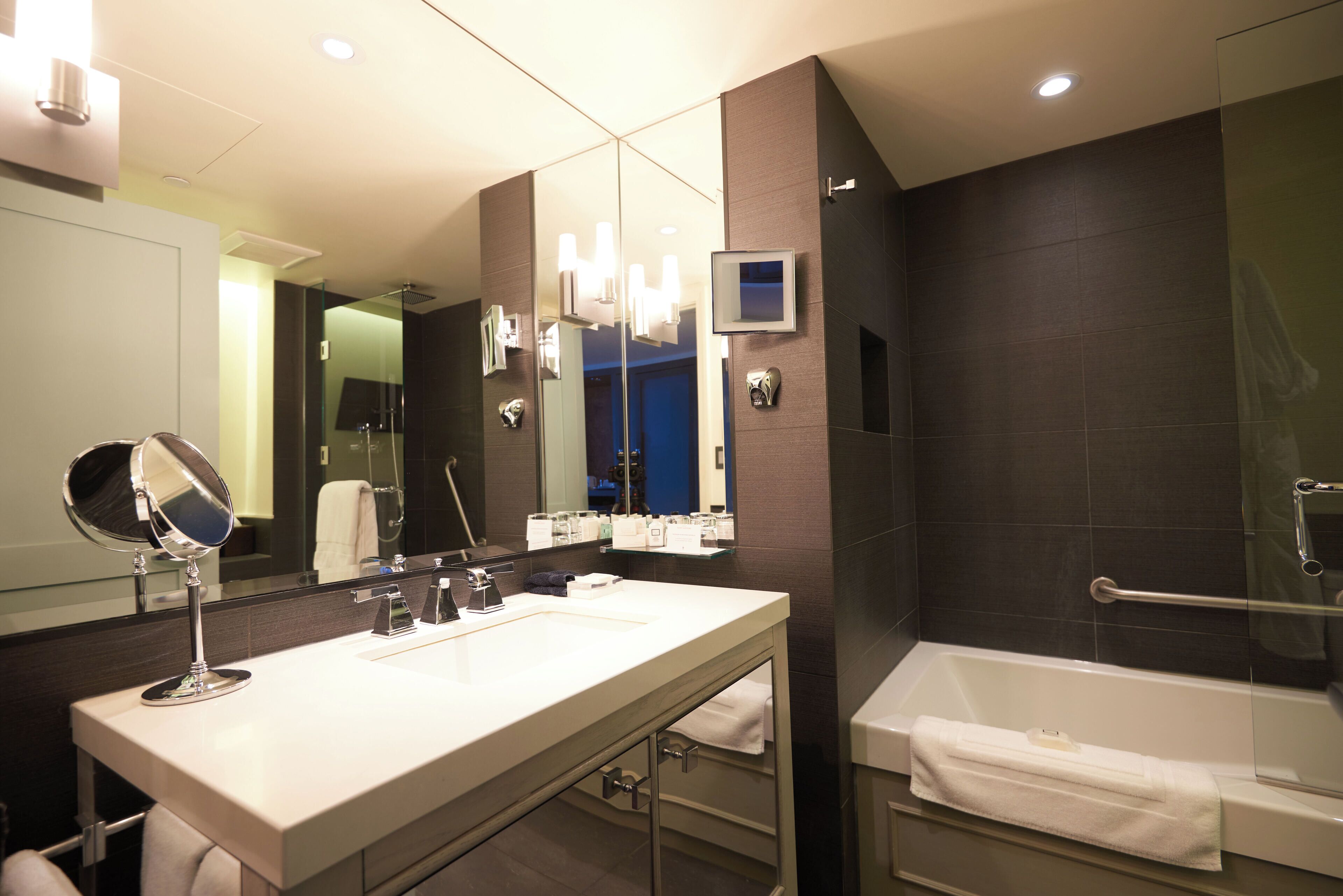 A modern bathroom with a large mirror, a vanity with a sink, a bathtub, and a shower area.