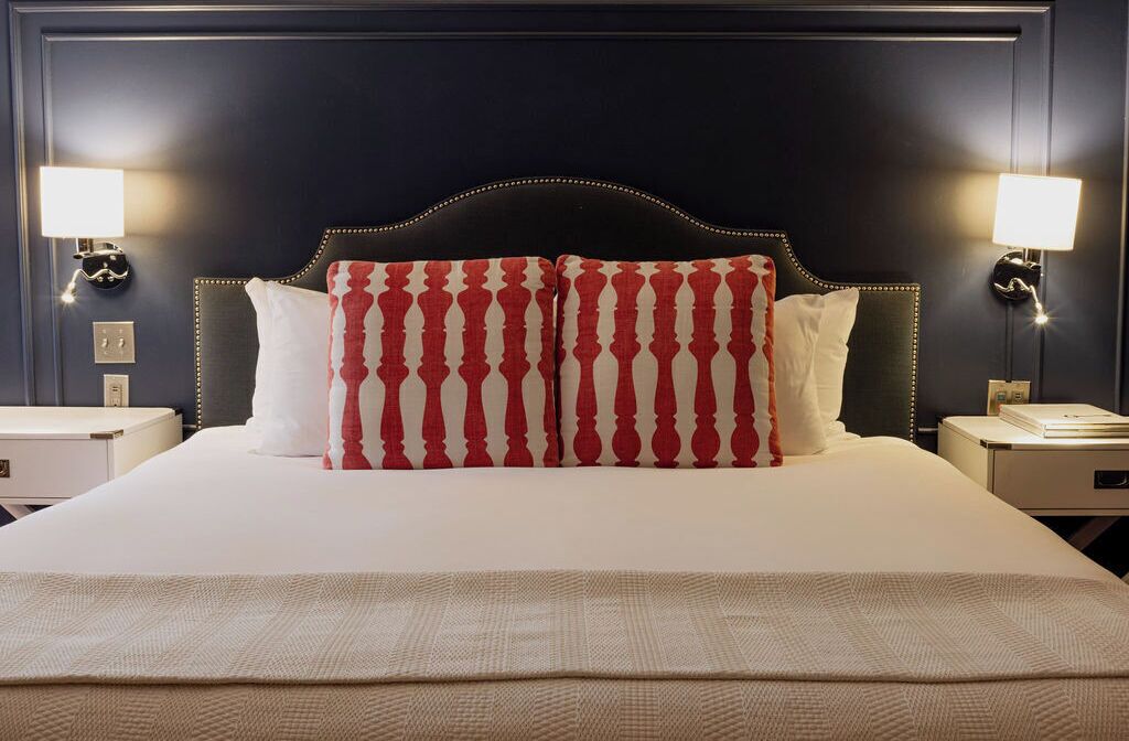 Una cama bien hecha con un cabecero oscuro y dos lámparas de noche.