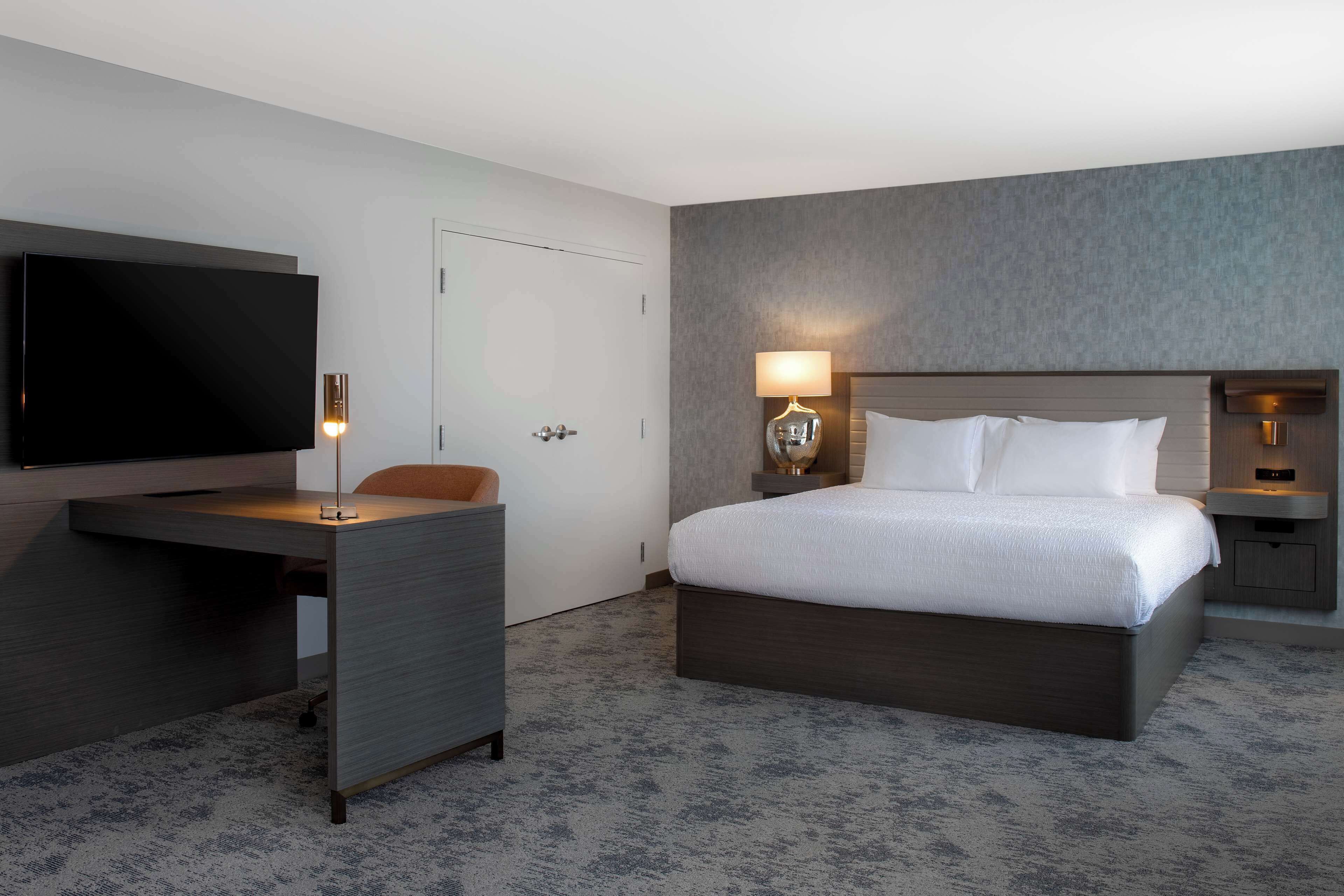Une chambre d’hôtel avec un lit, un bureau, une télévision et une lampe.