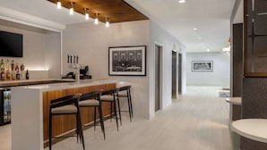 A modern bar area with a wooden counter, bar stools, and a mounted television. - Hampton Inn by Hilton Winnipeg Downtown (Winnipeg)
