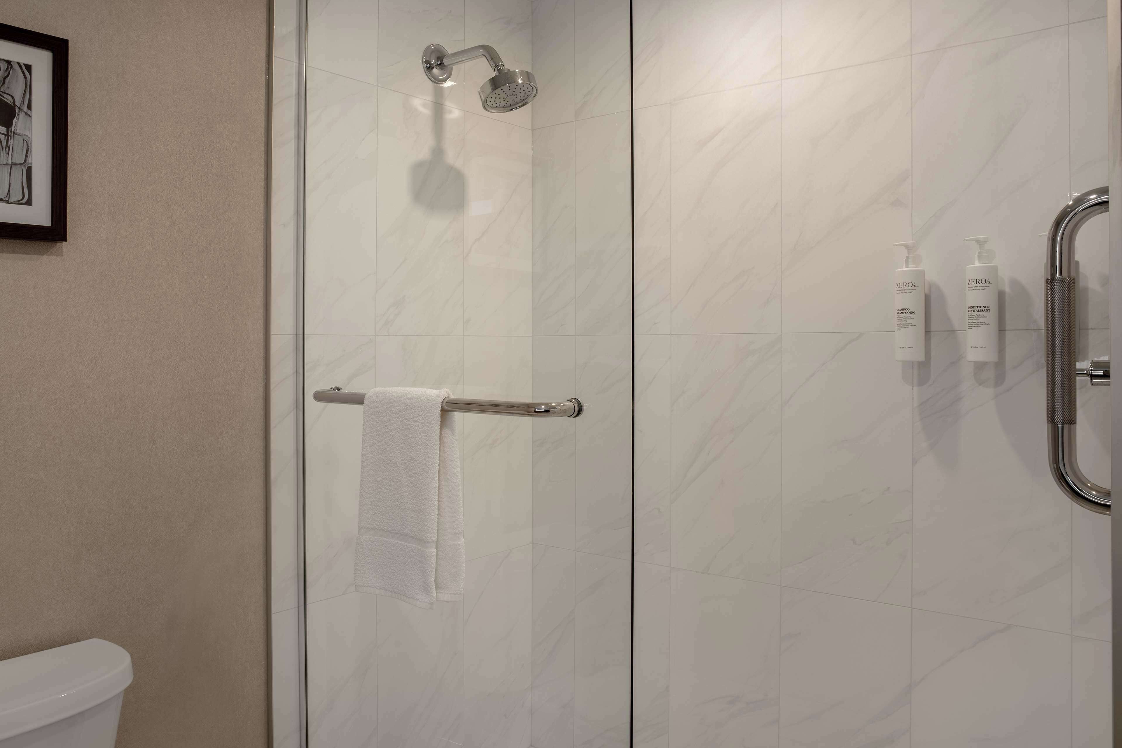 Un baño moderno con cabina de ducha de vidrio, un perchero y dos botellas de champú en la pared.