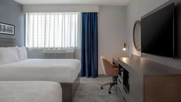 Une chambre d’hôtel avec deux lits, un bureau, une télévision et une grande fenêtre avec des rideaux.