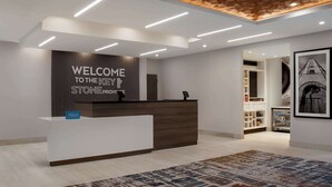 A hotel reception area with a modern design, featuring a reception desk, a "Welcome to the Key Stone Province" sign, and a view into the room service area. - Hampton Inn by Hilton Winnipeg Downtown (Winnipeg)