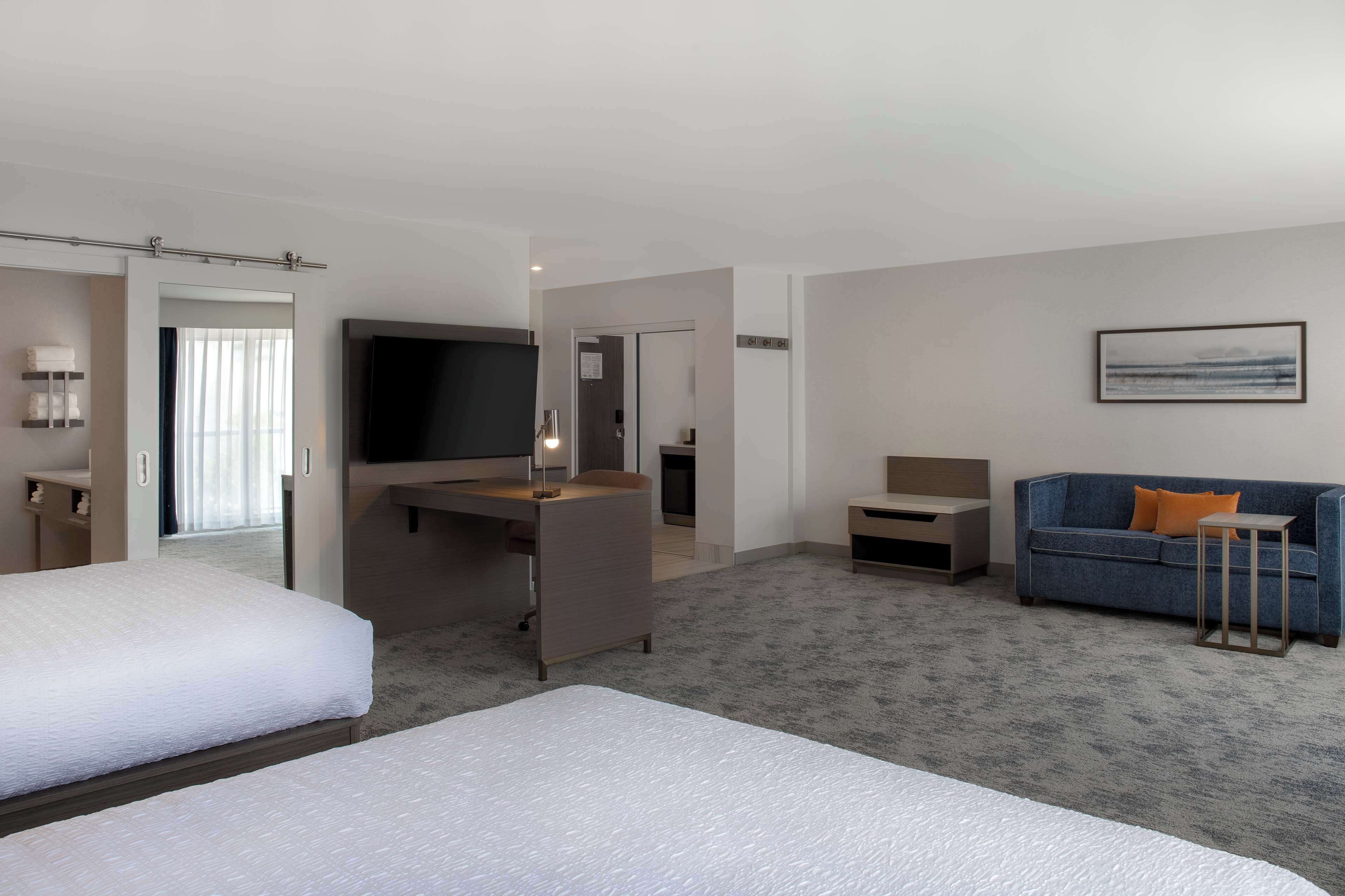 Habitación de hotel con dos camas, un escritorio, un sofá, un televisor y un cuadro en la pared.
