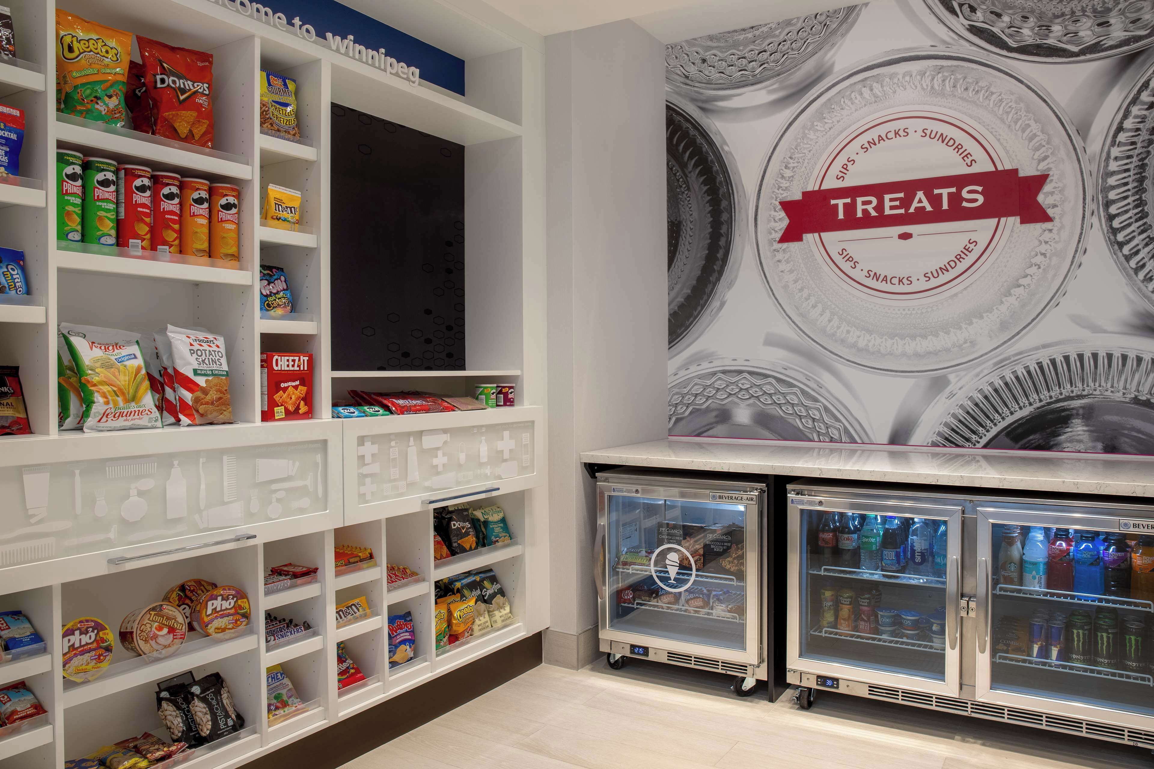 Zona de exhibición de aperitivos y bebidas con estantes llenos de diferentes opciones, y una sección refrigerada con bebidas.