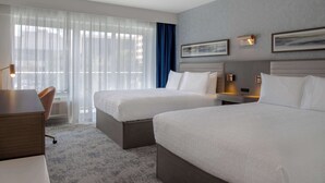 A hotel room with two beds, a desk, a chair, and large windows with sheer curtains. - Hampton Inn by Hilton Winnipeg Downtown (Winnipeg)
