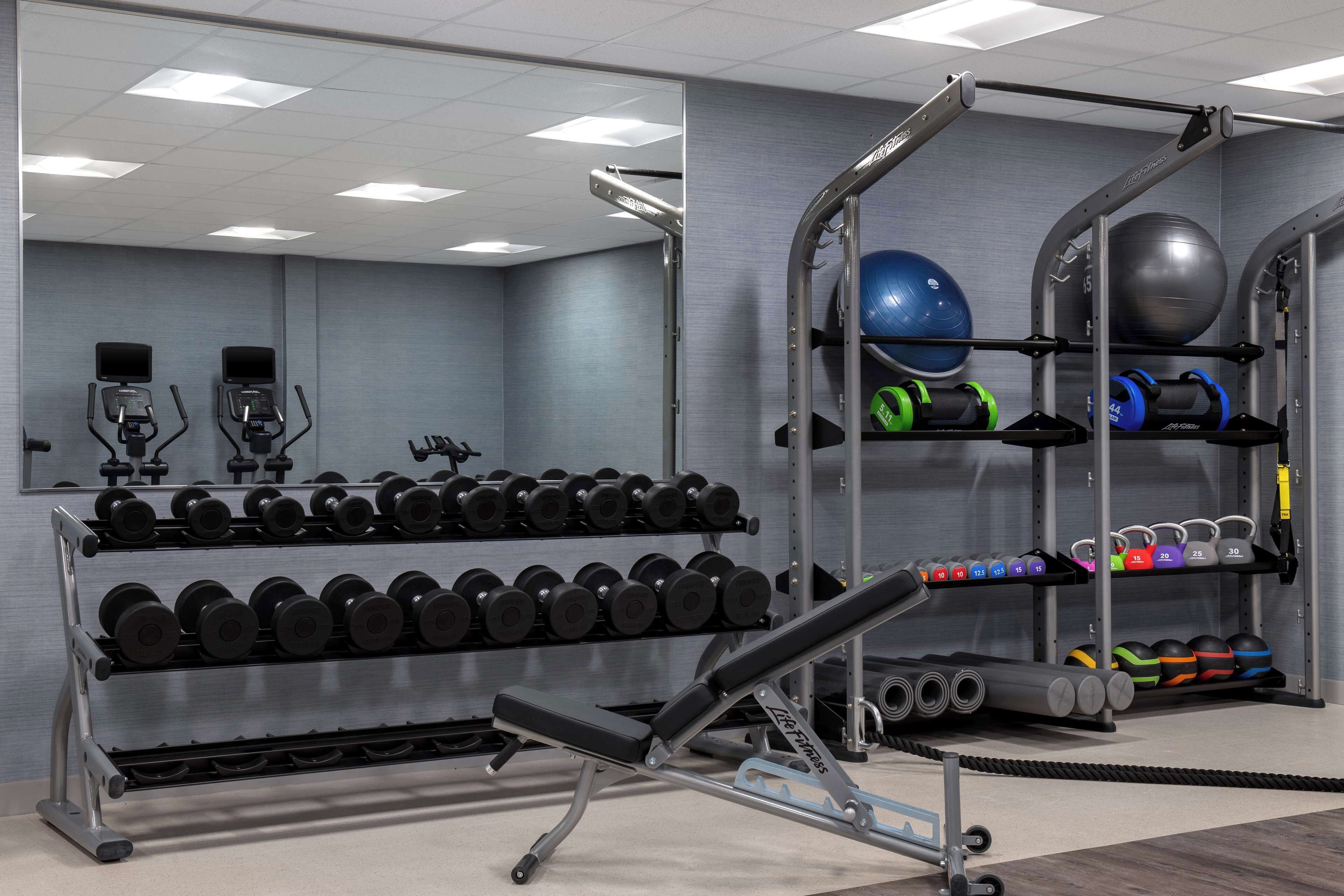 A gym with exercise equipment, including treadmills, dumbbells, and a bench.