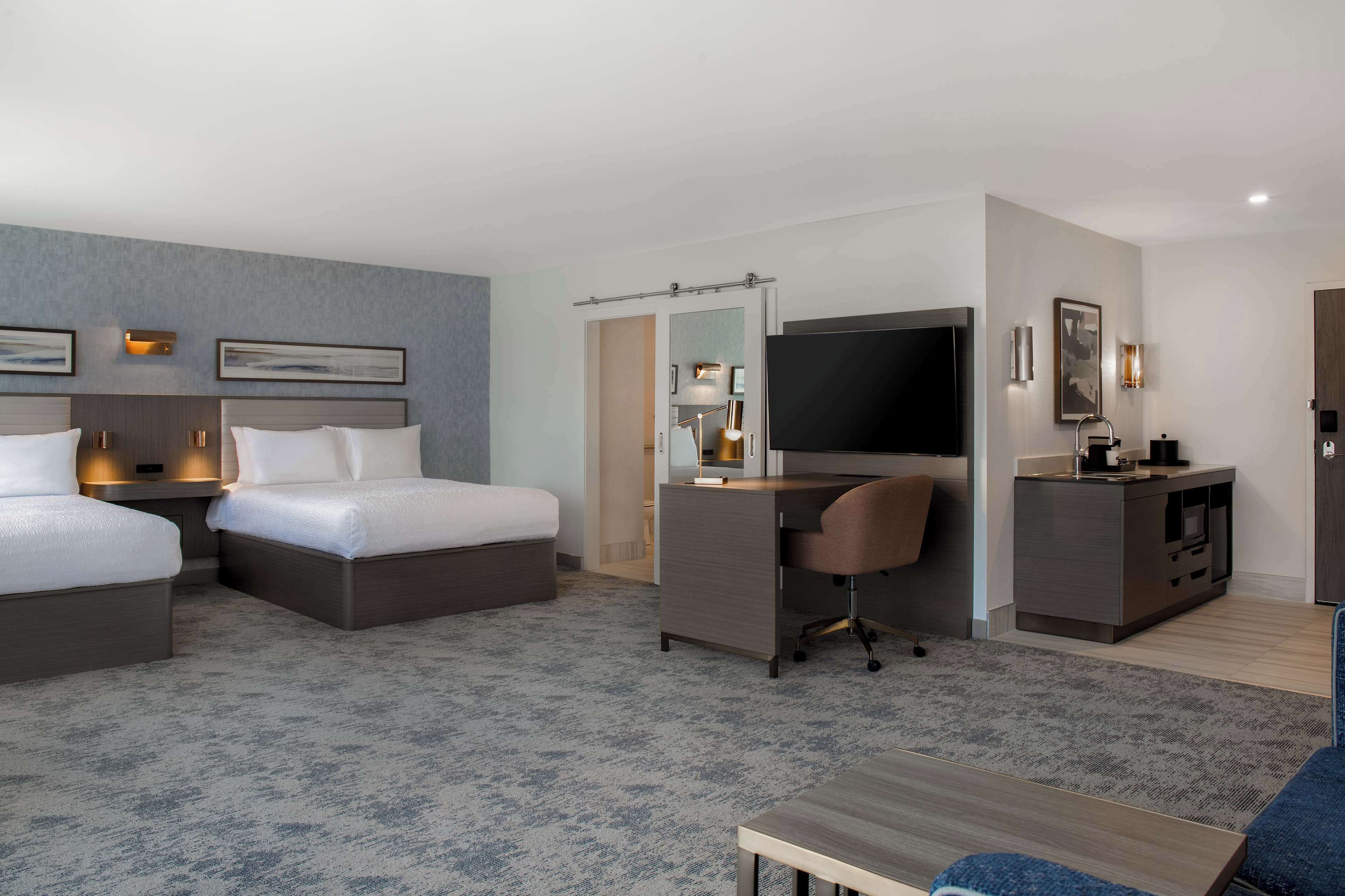 A hotel room with two beds, a desk, a television, and a small seating area.