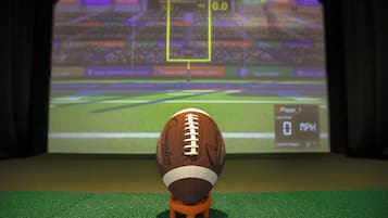 A football on a stand in front of a screen displaying a football game.