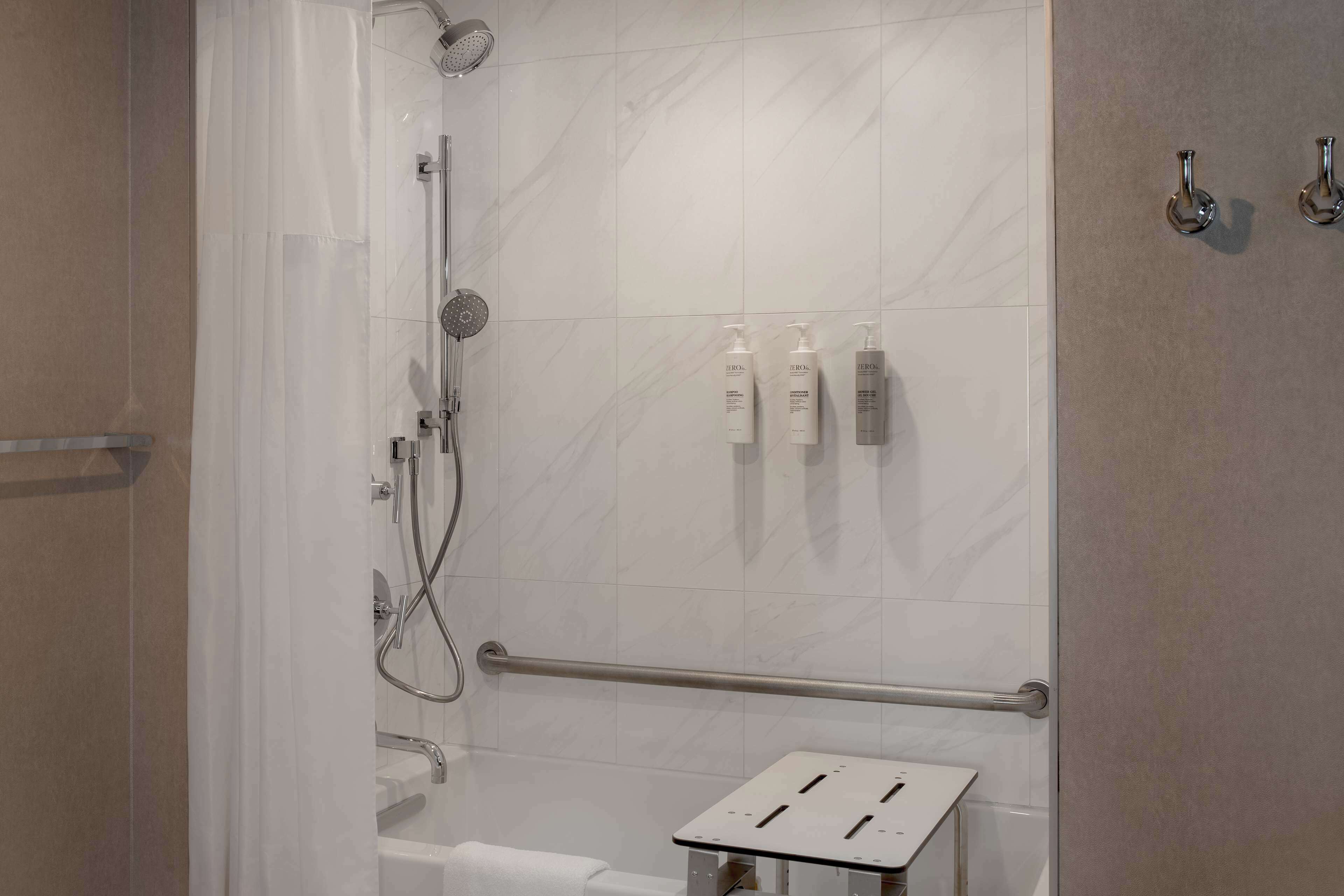 A modern bathroom with a shower, a grab bar, and toiletries on the wall.