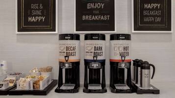 Un espace dédié au café, équipé de trois distributeurs de café étiquetés « café décaféiné », « café torréfié foncé » et « eau chaude ». On y trouve également des tasses à café et un panneau indiquant : « Bon appétit ».