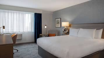 Una habitación de hotel con una cama grande, un escritorio, una silla, una lámpara y una ventana con cortinas.
