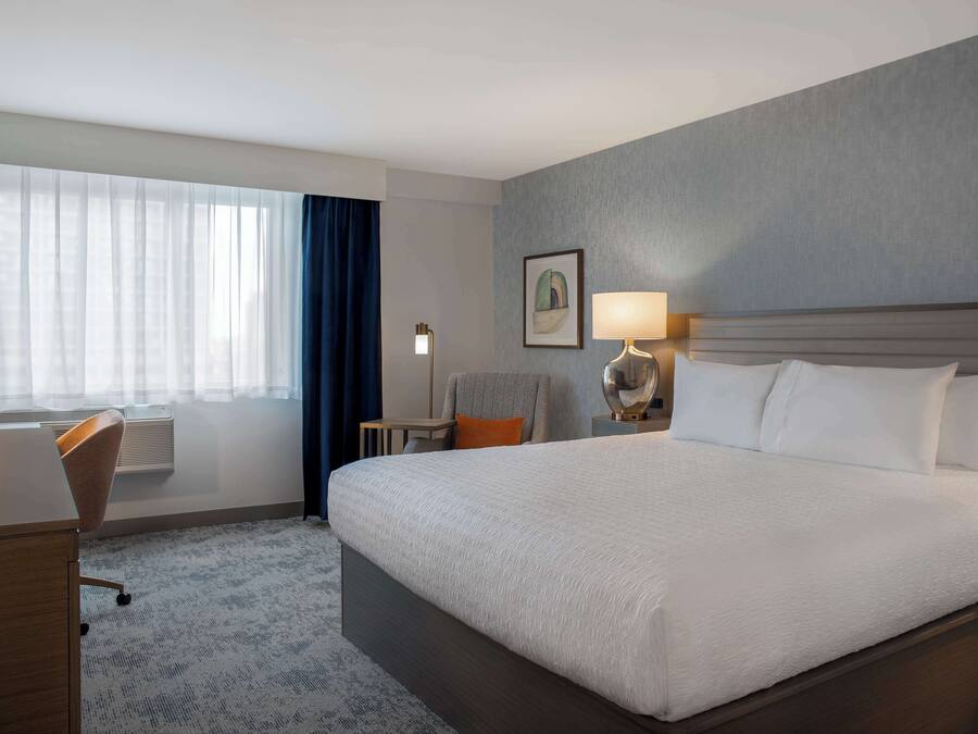 Una habitación de hotel con una cama grande, un escritorio, una silla, una lámpara y una ventana con cortinas.