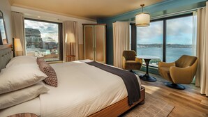 A hotel room with a large bed, two armchairs, a small table, and a view of the water.