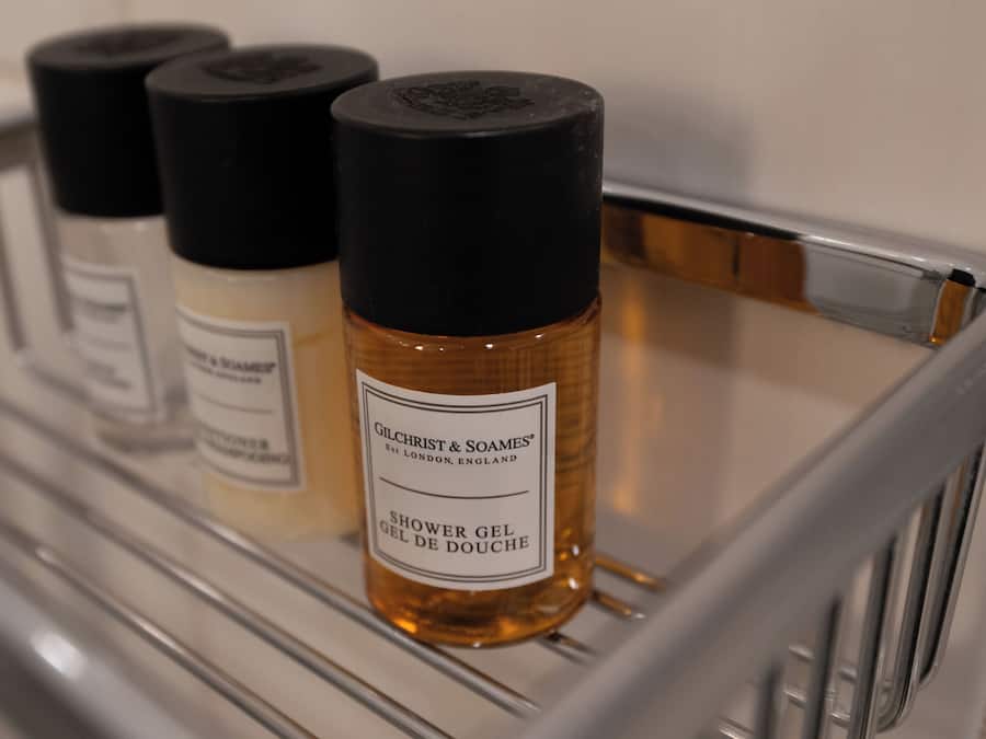 Une étagère de salle de bain avec trois bouteilles de gel douche Gilchrist & Soames.