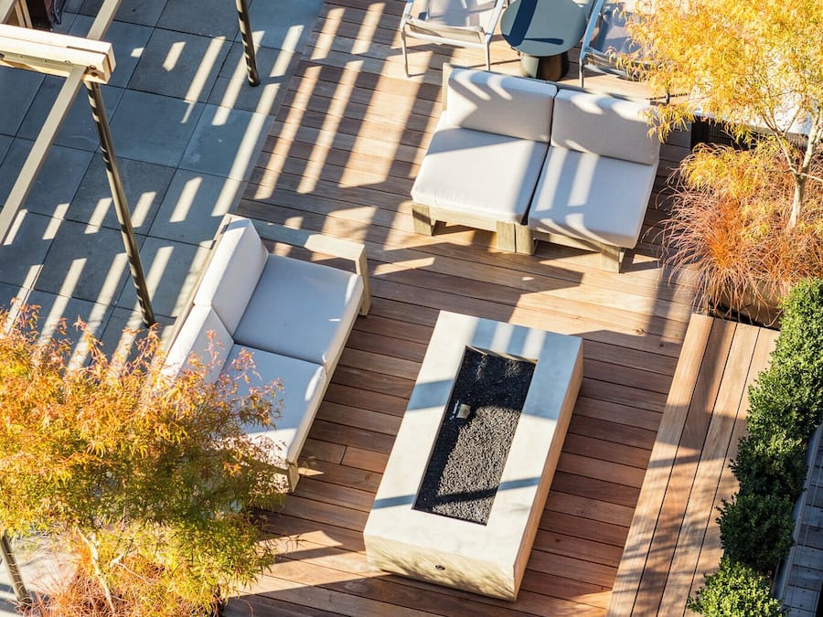 Un patio al aire libre con suelo de madera, asientos blancos acolchados y un hogar para la chimenea.