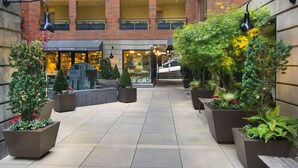 A courtyard with potted plants, a barbecue grill, and a building with a brick facade.