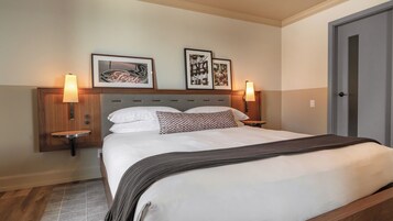 A neatly made bed with white linens and a patterned pillow, flanked by two wall-mounted lamps.