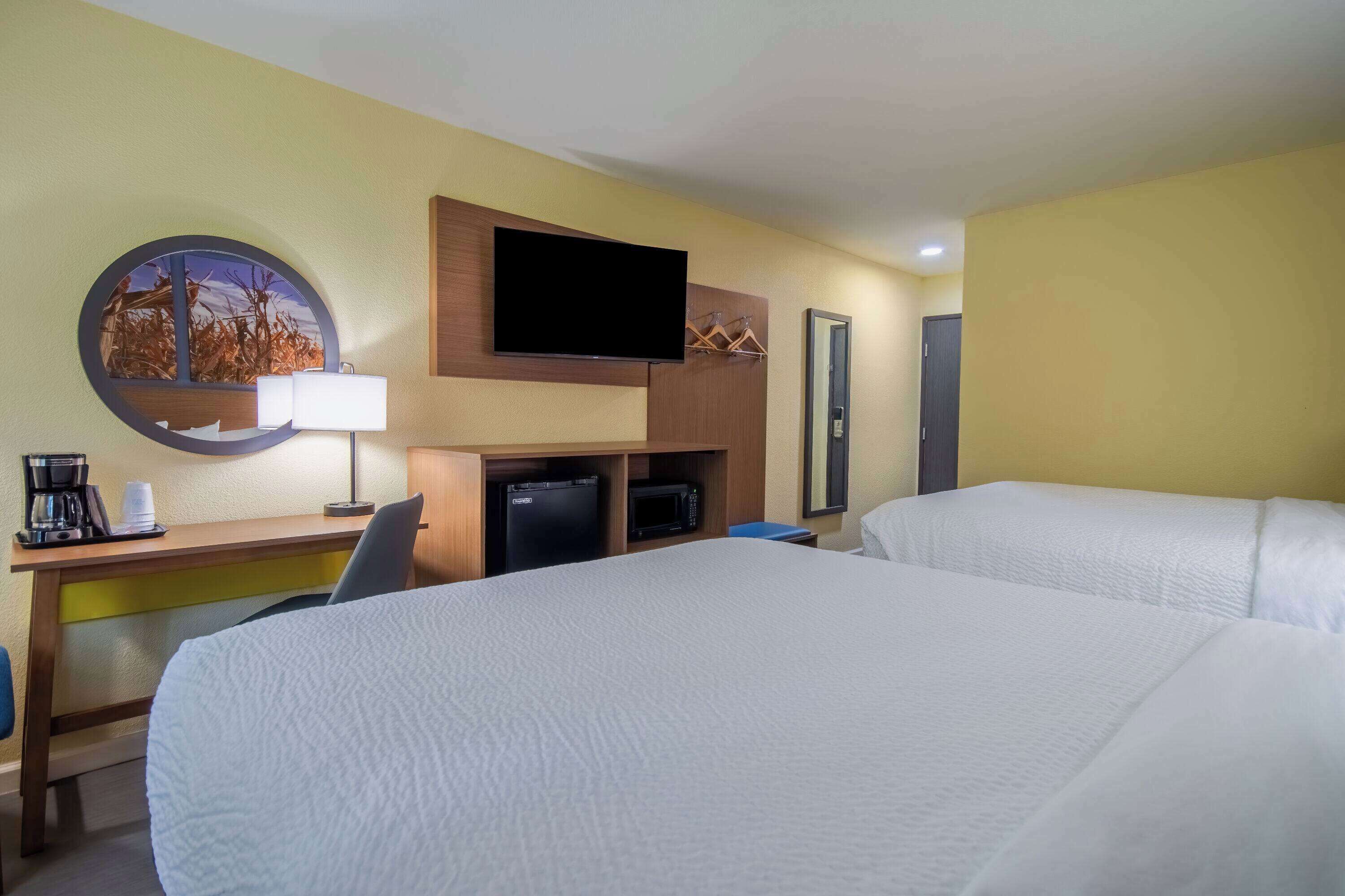 A hotel room with two beds, a desk with a flat-screen TV, a coffee maker, and a microwave.
