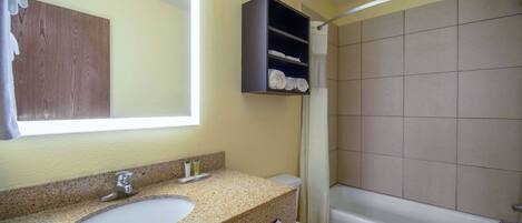 A bathroom with a sink, toilet, and bathtub. There is a shelf above the sink with towels.