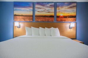 A hotel room with a large bed, a wooden headboard, and a sunset painting above the bed.