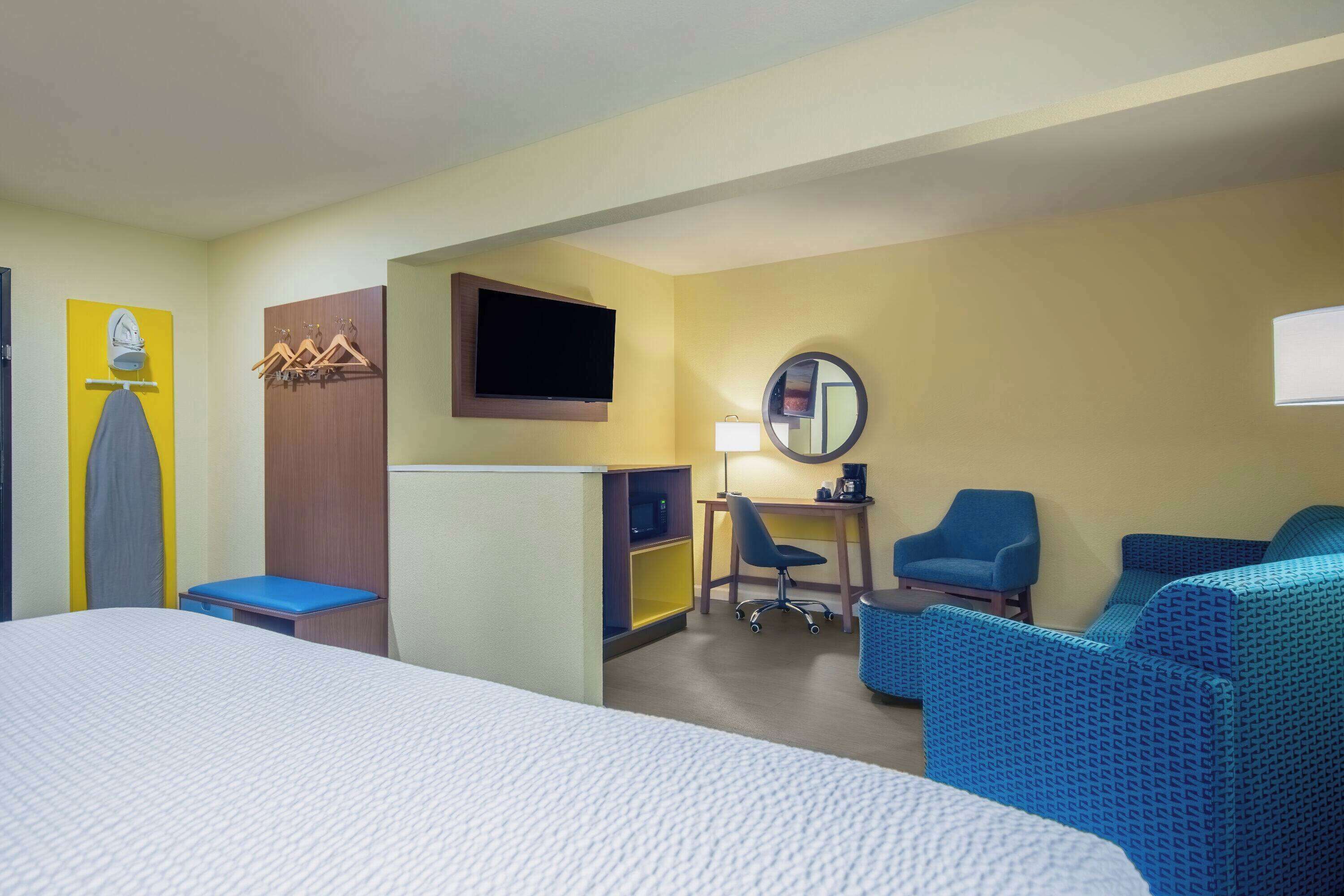 A hotel room with a bed, a desk, a chair, a sofa, a television, and a mirror.