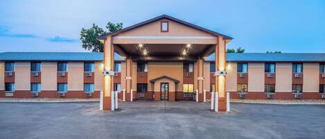 A multi-story hotel with a central entrance, a covered waiting area, and a parking lot.