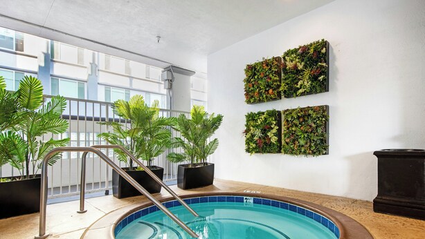 An indoor swimming pool with a metal ladder, surrounded by potted plants, and walls decorated with vertical gardens. - Peacock Suites (Anaheim)
