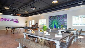 A room with a billiards table, a large peacock painting, and a dining area with tables and chairs. - Peacock Suites (Anaheim)