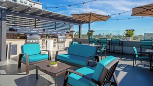 An outdoor patio with seating, a grill, and a view of the city. - Peacock Suites (Anaheim)