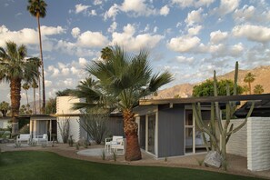 A modern house with a patio, palm trees, and a desert landscape.