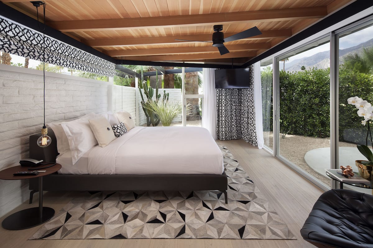 A modern bedroom with a large bed, a ceiling fan, and a view of the outdoors.