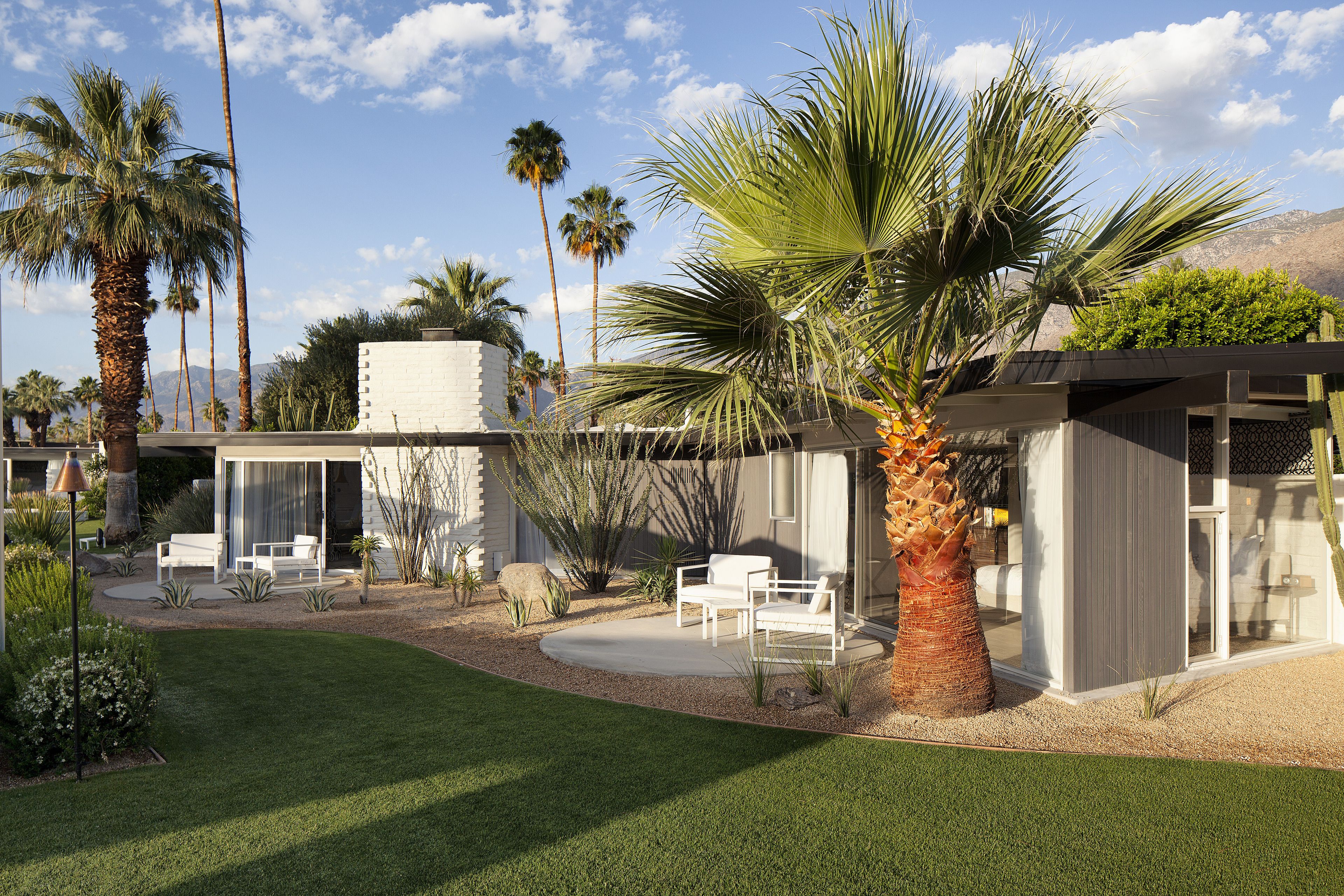 A modern house with a patio, white furniture, and palm trees.