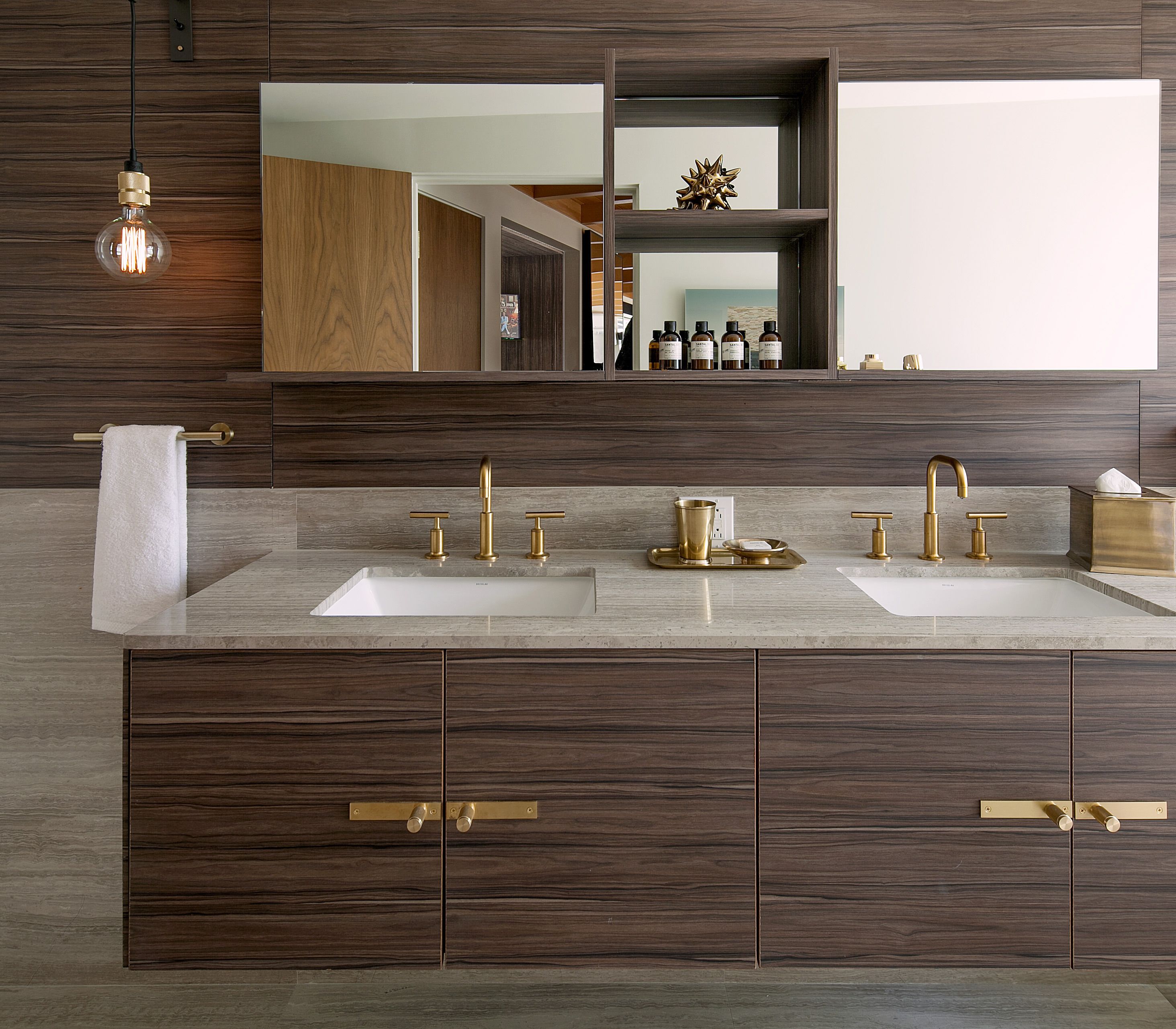 Une salle de bain moderne avec deux lavabos, des robinetteries dorées et un grand miroir au-dessus.