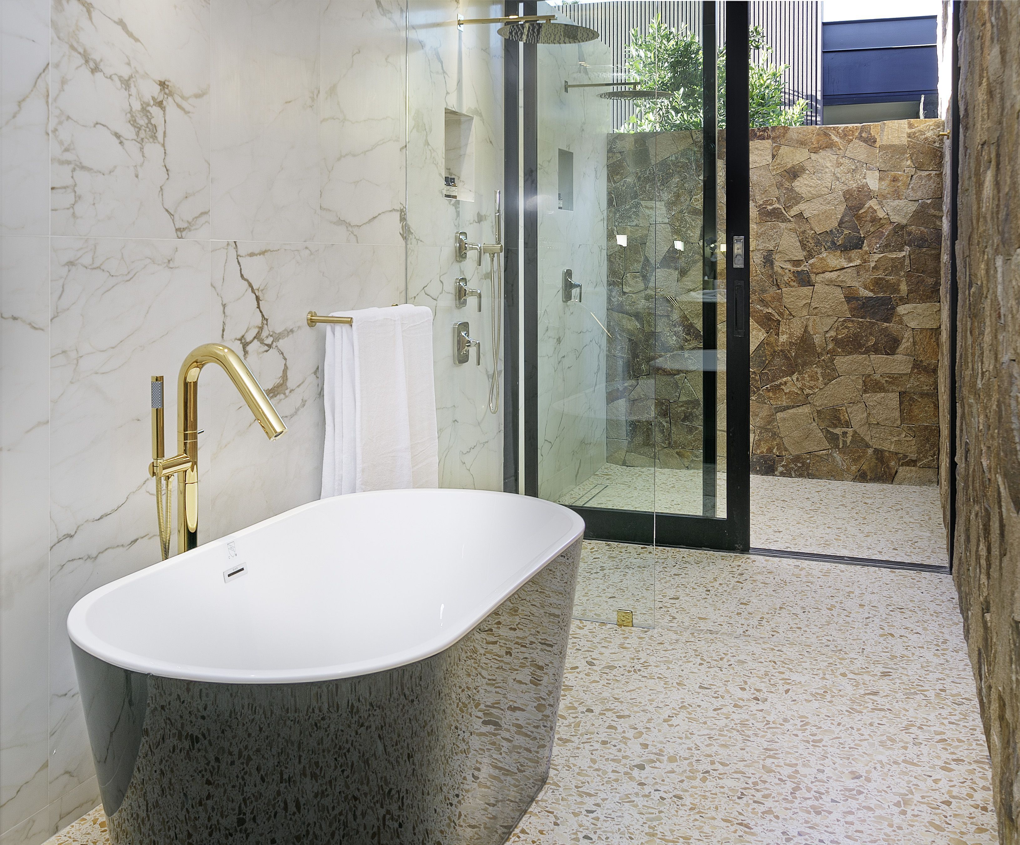 Ein modernes Badezimmer mit einer freistehenden Badewanne, einer gläsernen Duschkabine und einer Wand aus Stein.