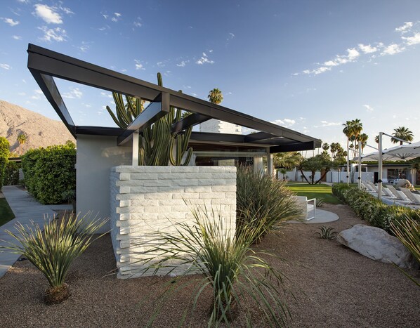 A modern house with a stone wall, a pergola, and a well-maintained garden with cacti and palm trees. - L'Horizon Resort & Spa, Hermann Bungalows (Palm Springs)