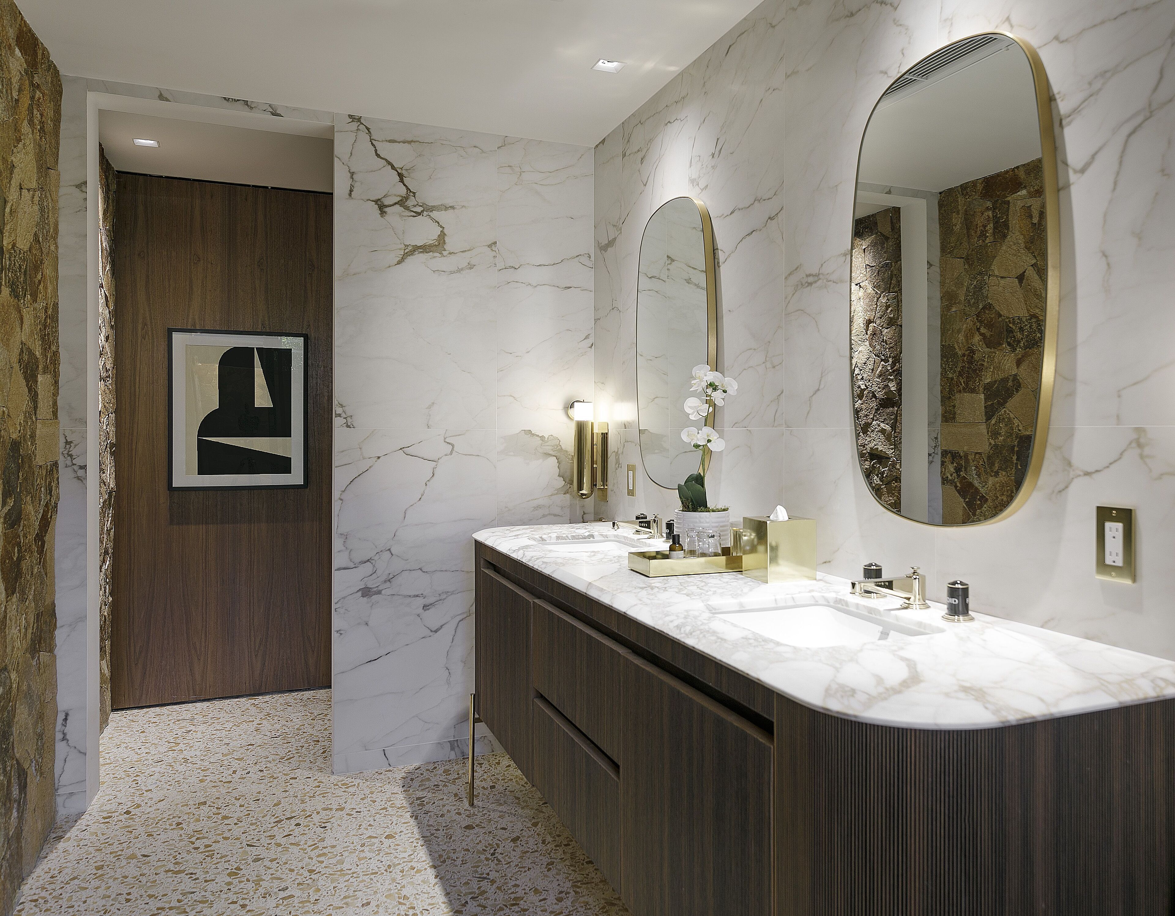 A modern bathroom with a marble vanity, a large mirror, and a framed artwork on the wall.