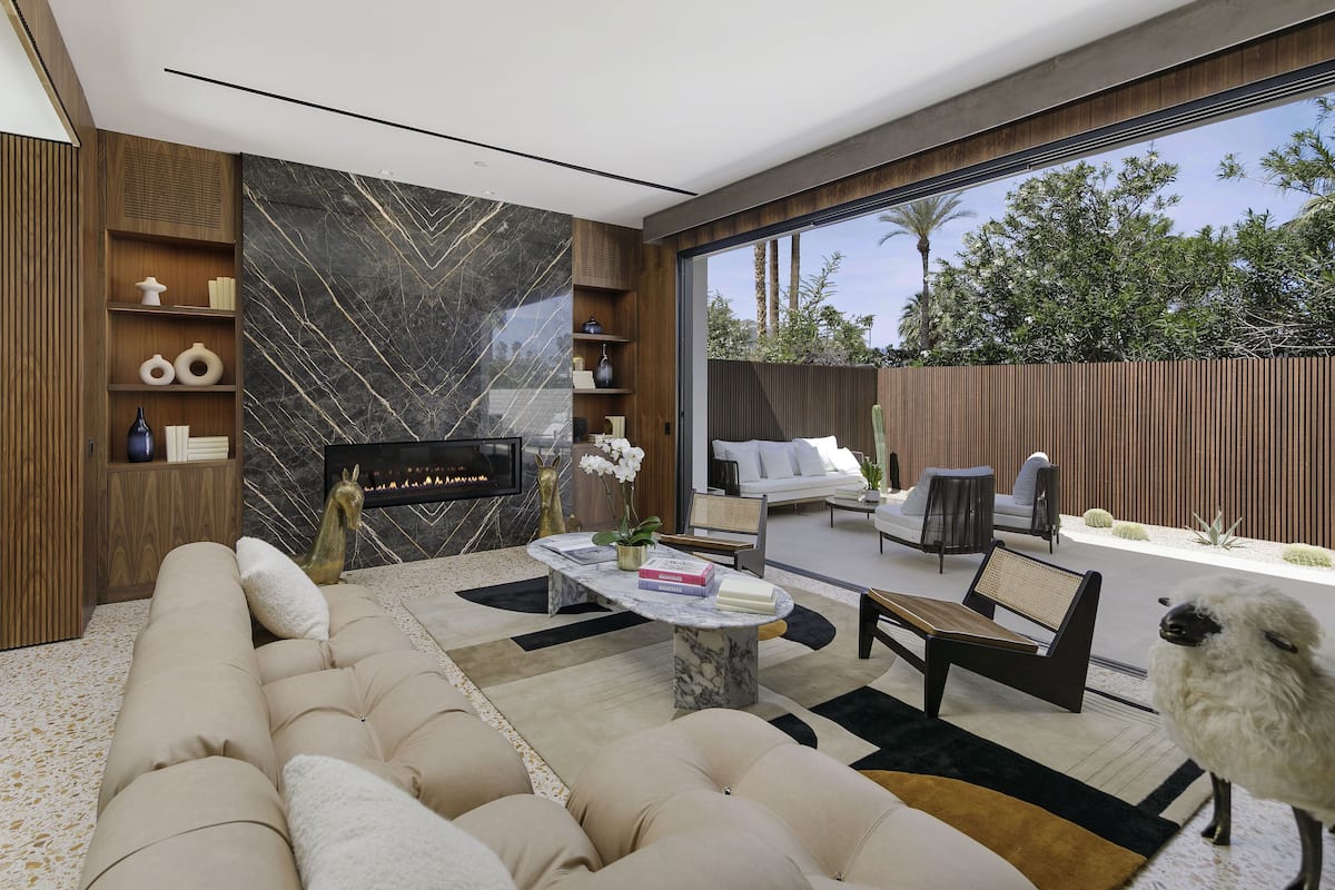 A modern living room with a fireplace, comfortable seating, and a large window overlooking a garden.