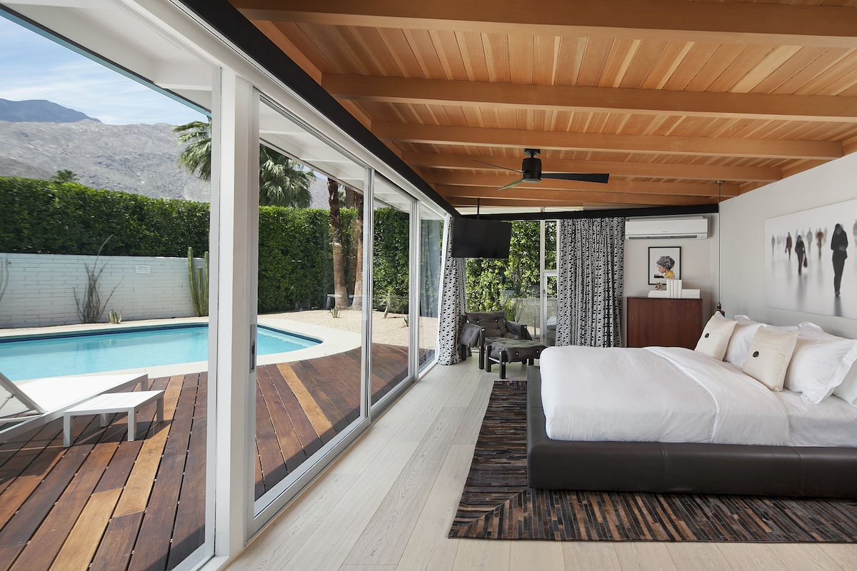A bedroom with a large bed, a view of a swimming pool, and a ceiling fan.