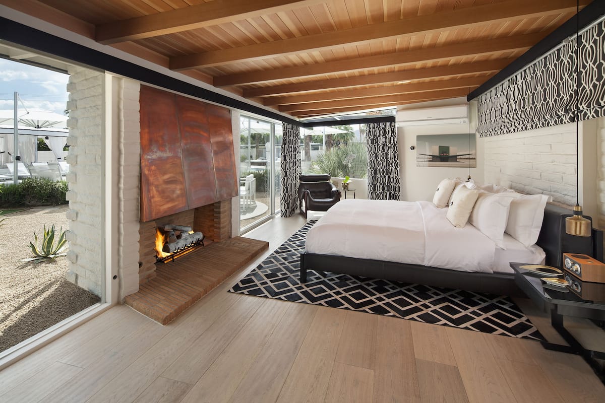 A modern bedroom with a large bed, a fireplace, and a view of the outdoors.