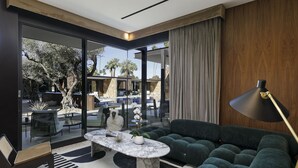 A modern living room with a glass wall, a plush green sofa, a marble coffee table, and a large floor lamp. - L'Horizon Resort & Spa, Hermann Bungalows (Palm Springs)