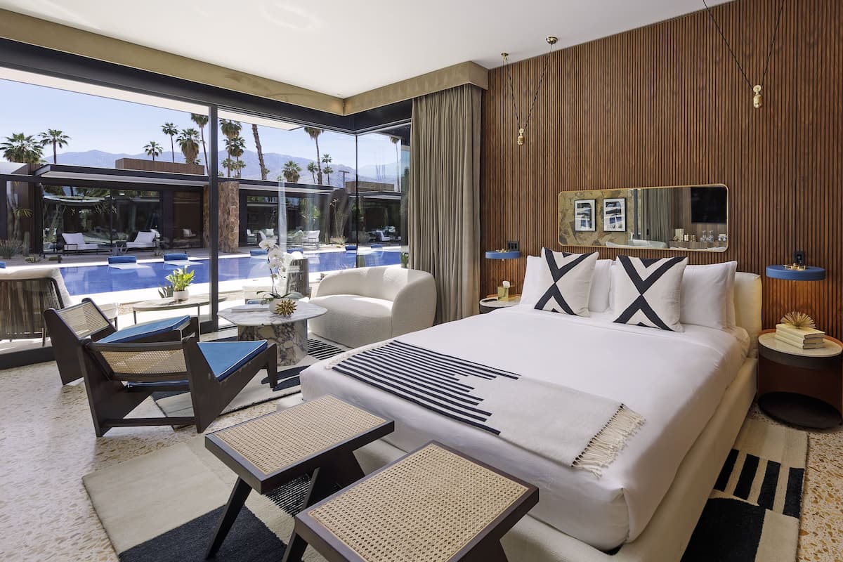 A modern hotel room with a large bed, a seating area with a pool view, and a television on the wall.