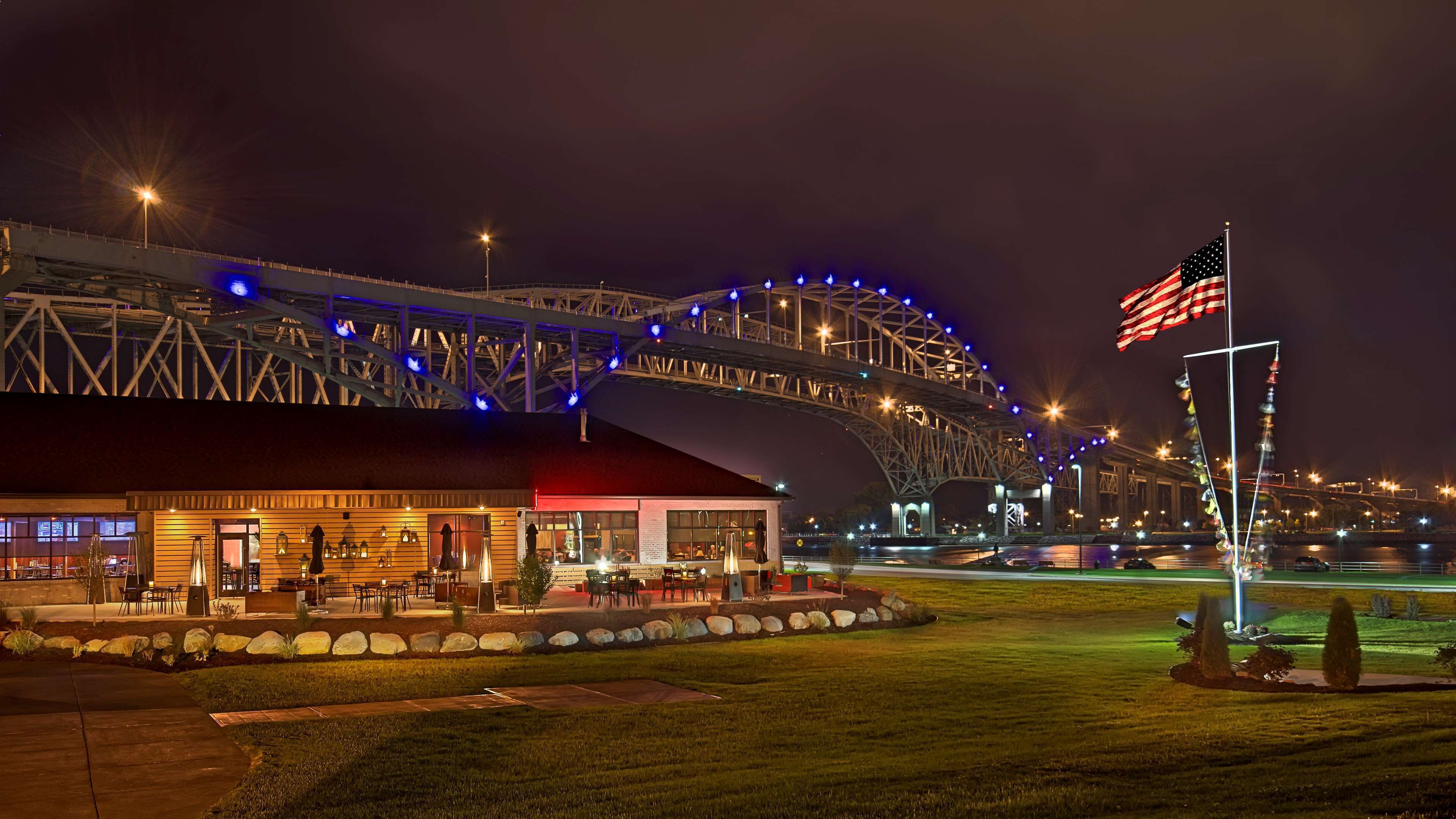 A stadium with a large American flag, a covered seating area, and a building with outdoor seating.