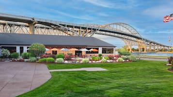A building with a covered patio area, a lawn, and a view of a large bridge structure in the background.