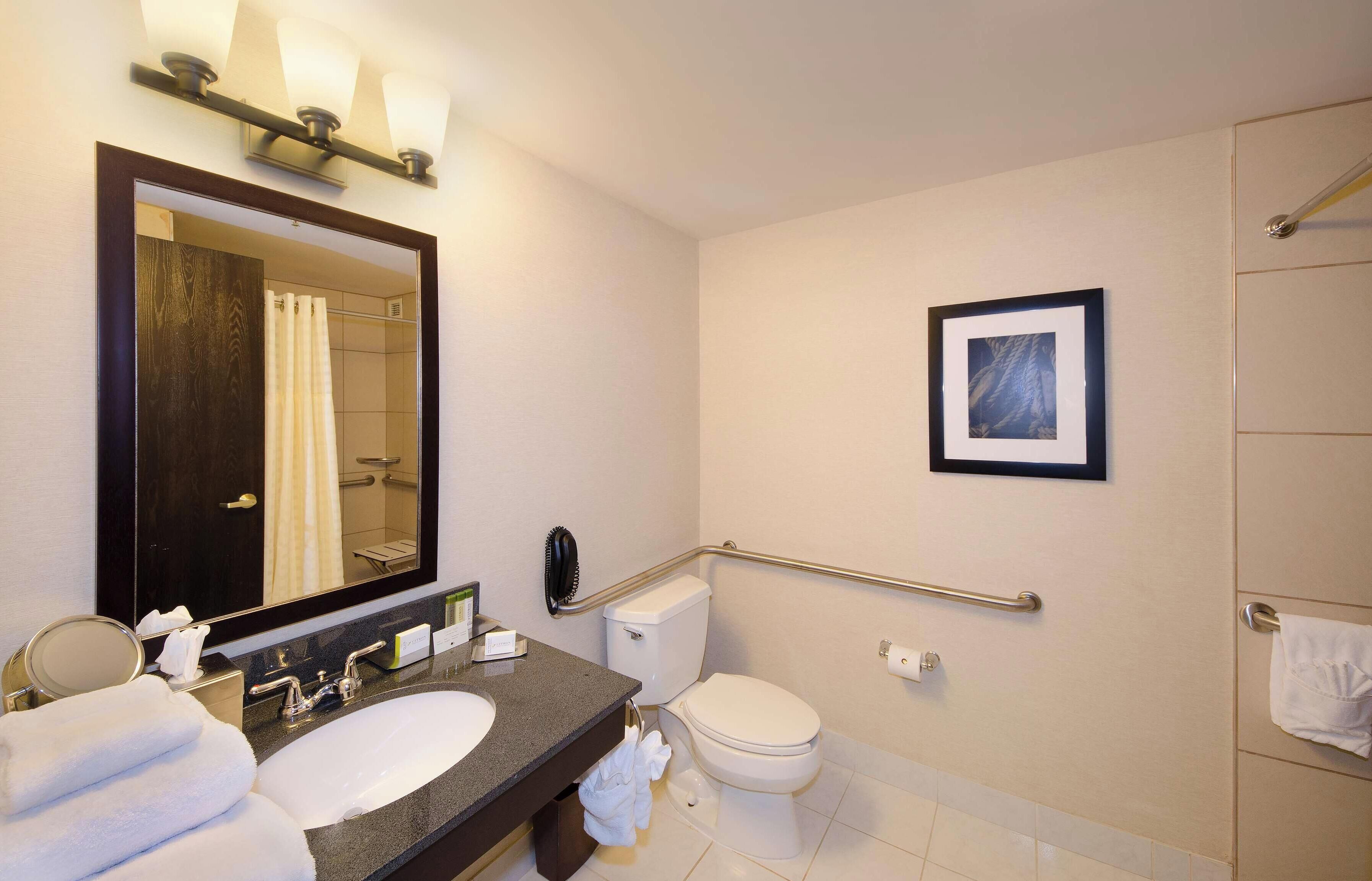 A modern bathroom with a large mirror, a sink, a toilet, and a shower.