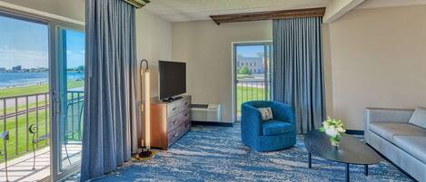 Una habitación de hotel con balcón, televisión, sofá, sillón y una mesita.