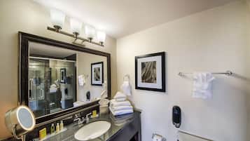 Un baño moderno con un espejo grande, un lavabo y una tocador. Hay toallas colgadas en un perchero, un cuadro en la pared y un teléfono en la encimera.