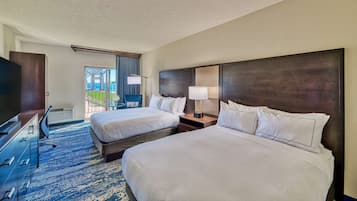Habitación de hotel con dos camas, un escritorio y un televisor. Cuenta con un balcón con vista al océano.